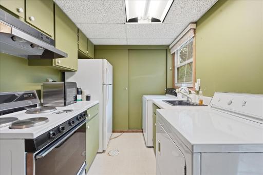 Versatile lower-level laundry room featuring a convenient second kitchen with stove, refrigerator, sink, cabinetry, and counter space.