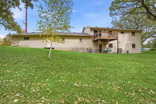 Rear exterior view showcasing the expansive backyard, mature trees, upper-level deck, and lower-level patio with convenient access to the home.