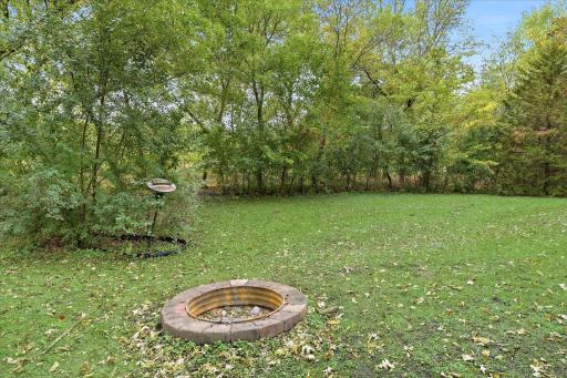 Private backyard fire pit area tucked alongside mature trees, an inviting spot to gather and enjoy the wooded surroundings.