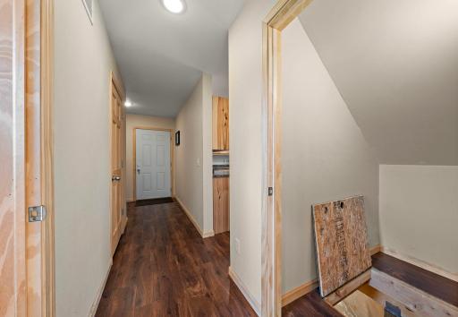 Main floor hallway with open doorway to bathroom, garage door access down the hall beyond and crawl space access through the trap door under the staircase.