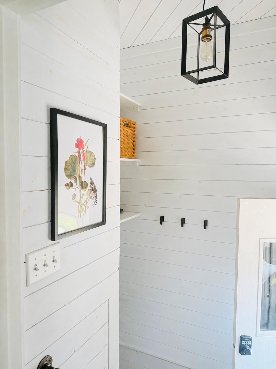The back entryway has shiplap and new lighting. There are hooks for coats, a shoe rack, and above the stairway storage.