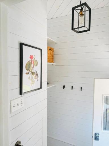 The back entryway has shiplap and new lighting. There are hooks for coats, a shoe rack, and above the stairway storage.