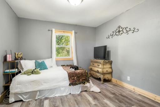 A comfortable bedroom with updated flooring, neutral finishes and a large window overlooking the wooded surroundings.