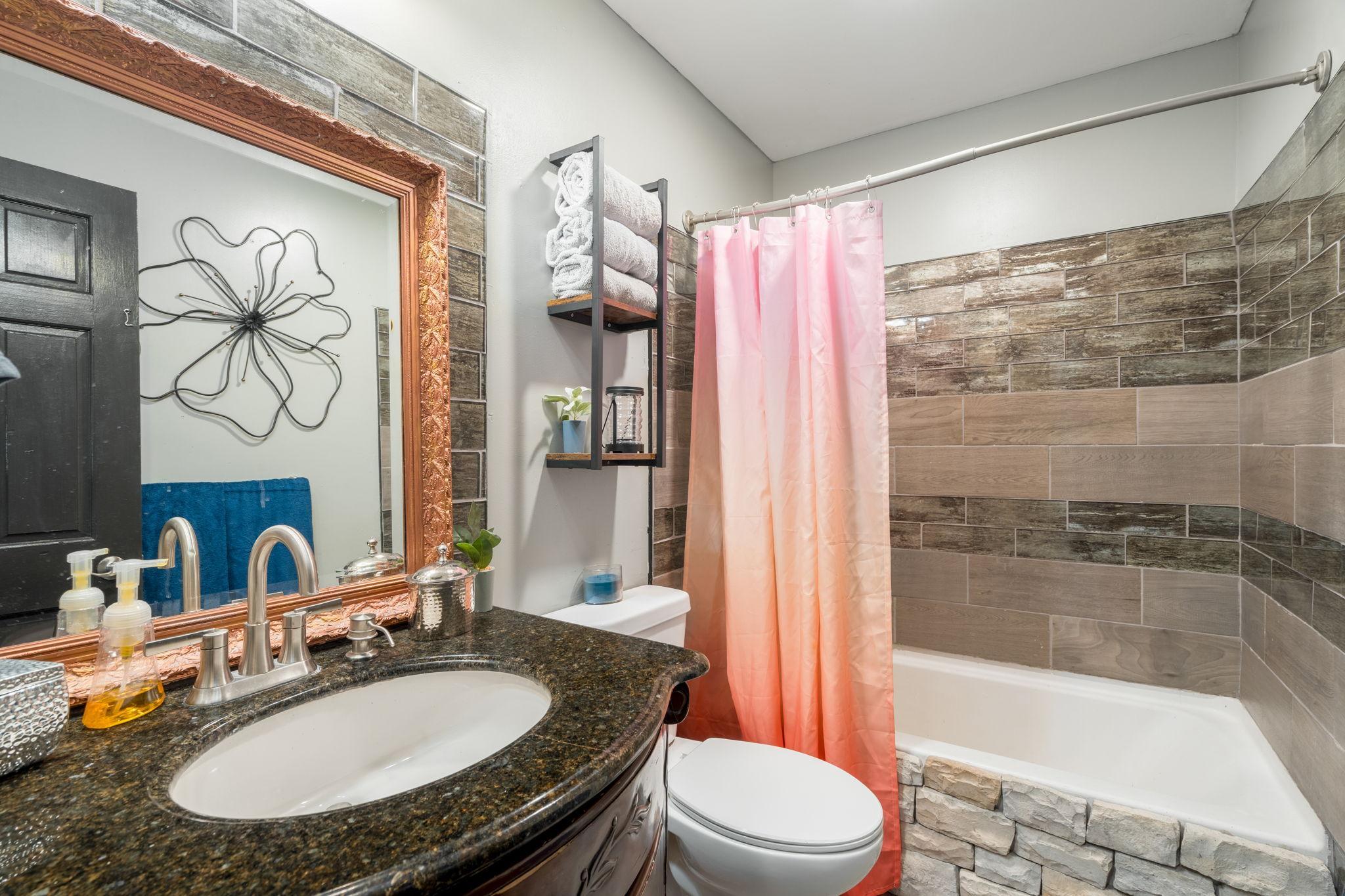 Updated bathroom featuring a granite vanity, decorative tile surround and tub/shower combination.