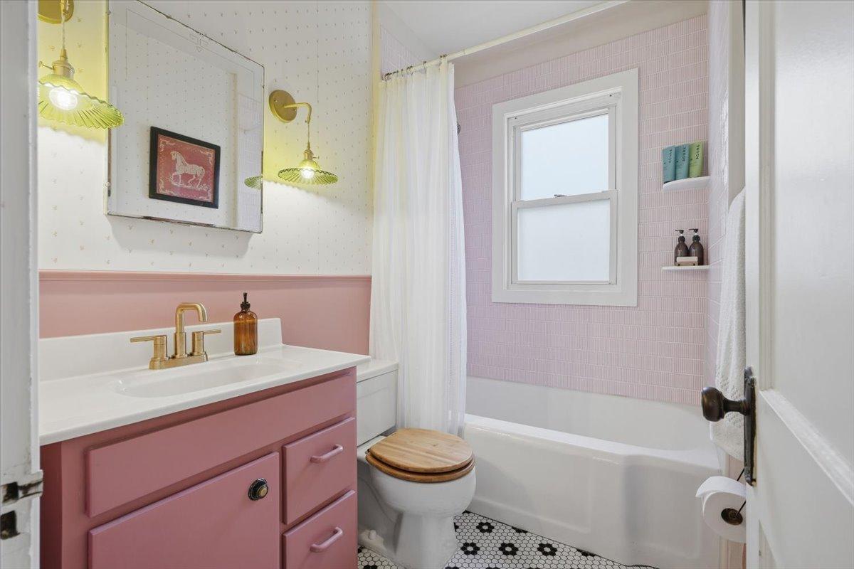 A little color goes a long way. The updated full bathroom pairs playful pink tones with brass finishes and classic black-and-white flooring.