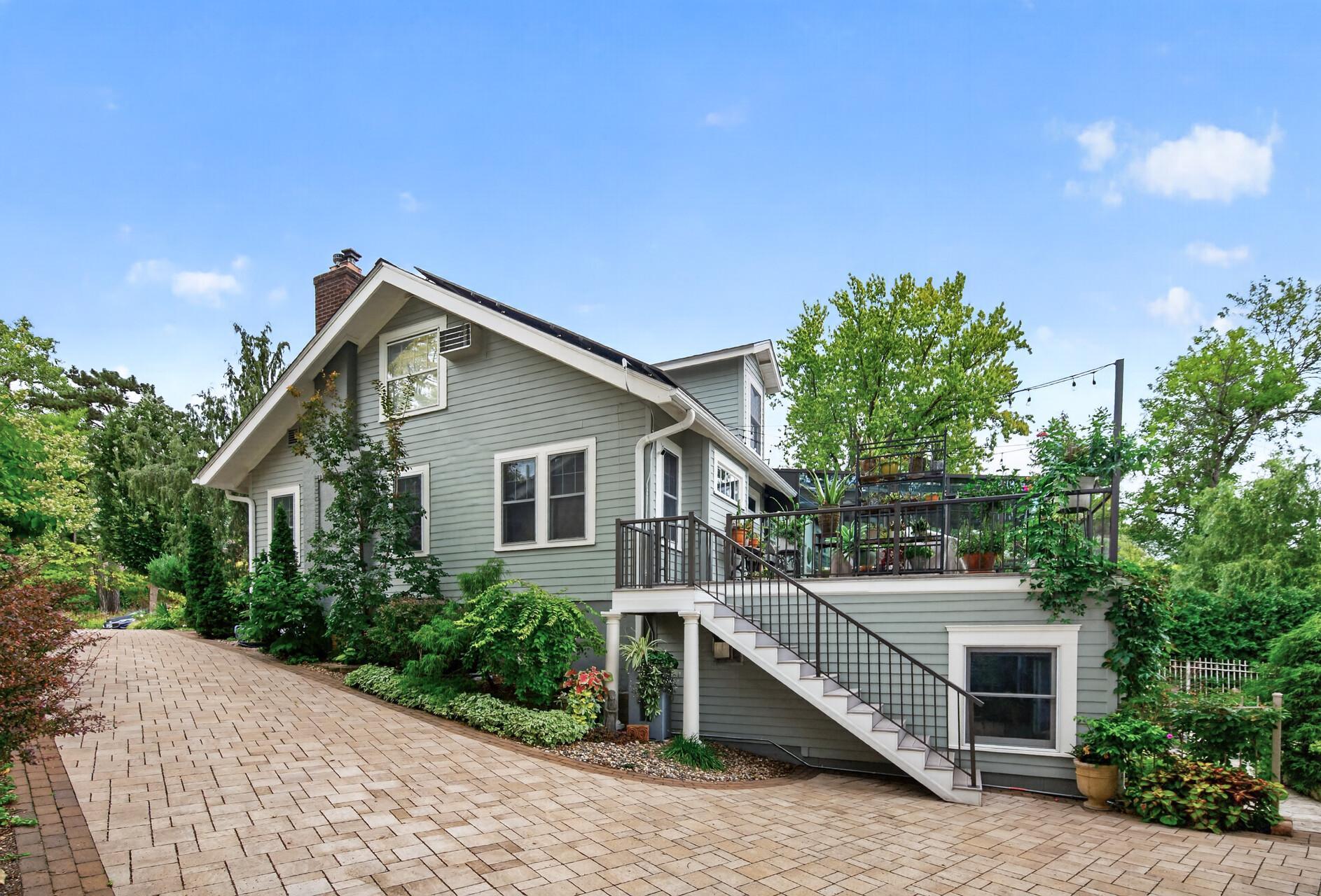 Side and rear view showcasing the paver driveway and stairs to the expansive deck.