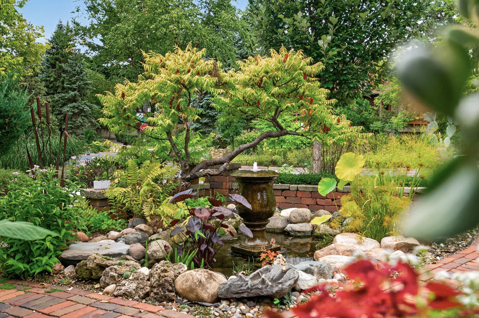 Artfully designed landscaping brings together a tranquil pond, vintage brick, natural boulders, groundcover and sculptural trees in one beautifully cohesive garden scene.