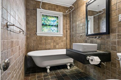 Tiled floors and walls, a sleek sink, and a classic clawfoot tub with shower head create a charming upper level full bath, complete with a bright window.