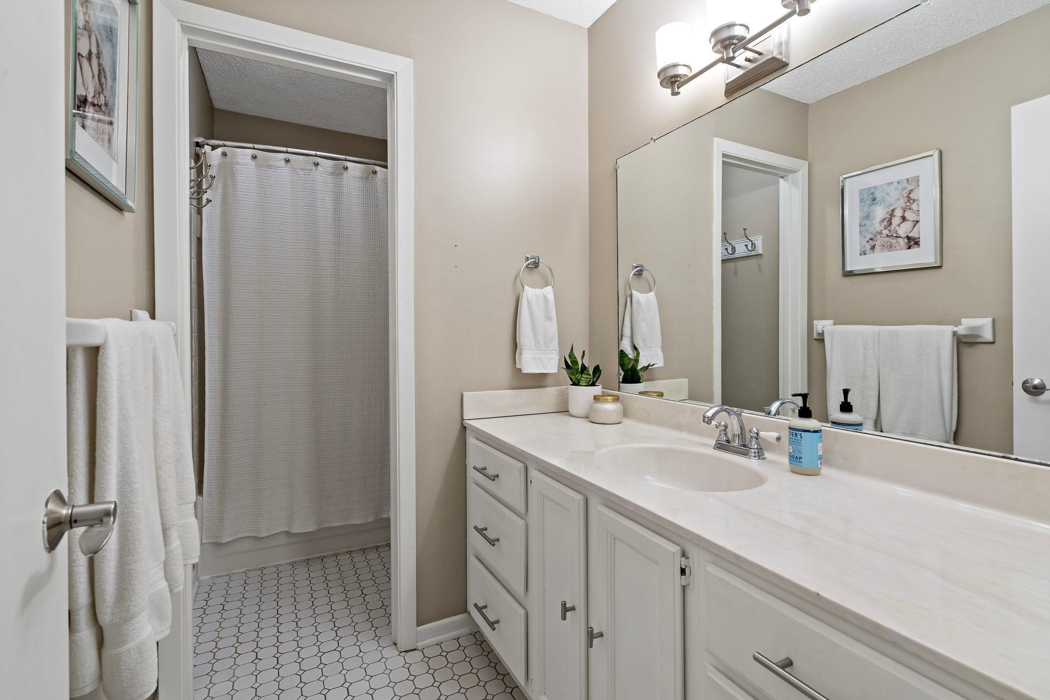 The upper-level full bathroom features a functional split layout with tile flooring, generous counter space and ample vanity storage. A separate tub/shower area with tile surround adds privacy and convenience to the space.