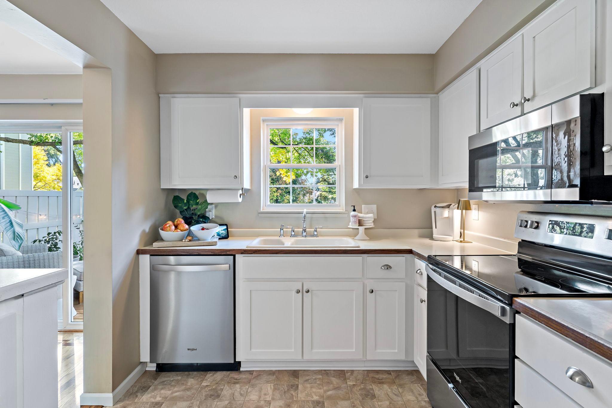 Natural light pours through the kitchen window above the sink, offering a lovely view of the surrounding greenery. Crisp white cabinetry, generous counter space, and a convenient layout create a bright and functional space for everyday cooking.