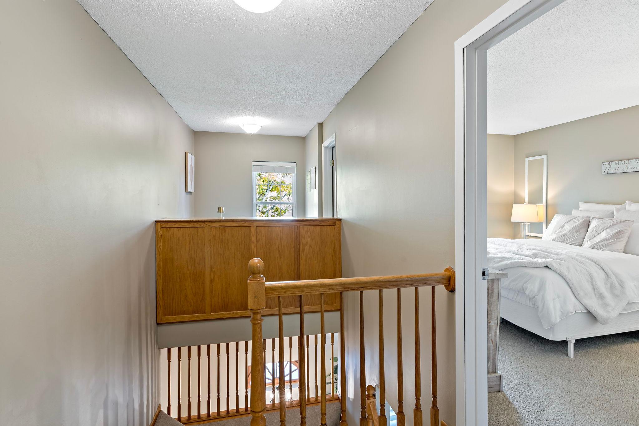 The upper-level landing connects both bedrooms, the full bathroom and bonus flex space, with an open railing overlooking the entry below and a window bringing natural light into the hallway.
