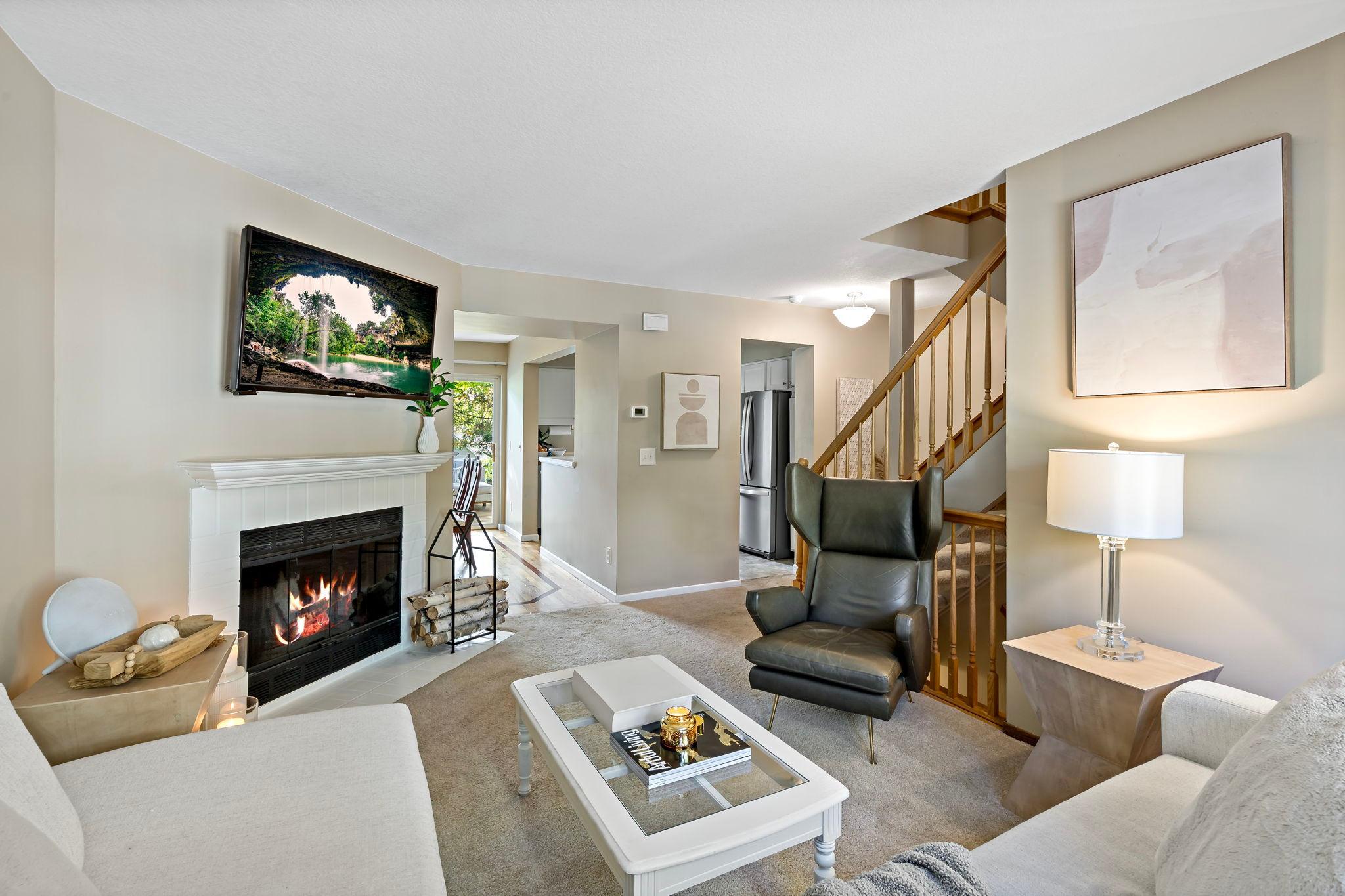 A second view highlights the living room's wood-burning fireplace with a classic white mantel & brick surround. The thoughtful layout offers easy access to the adjoining dining area & kitchen, creating a natural flow between the home's living spaces.