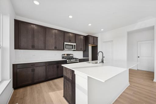 This stylish kitchen features rich cabinetry, quartz countertops, stainless steel appliances, and a large island-perfect for cooking, dining, or entertaining. Home under construction, photo of similar home, selections vary.