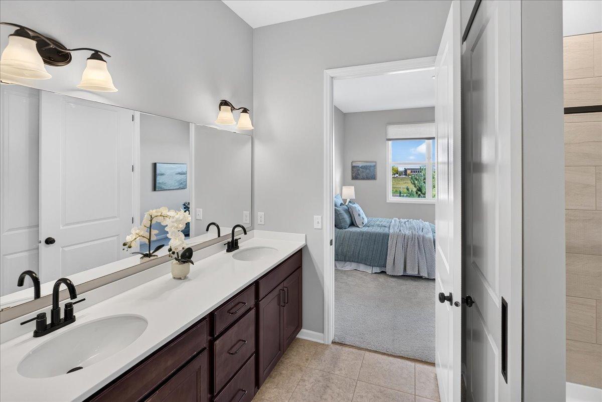 Spacious private bath featuring a double-sink vanity, attractive cabinetry, and direct access to the primary bedroom.