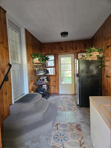 Convenient entryway featuring warm wood-paneled walls, tile flooring, and direct access to the home and outdoors.