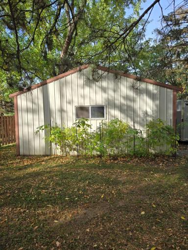 Detached pole building with metal siding and a window, surrounded by mature trees and established greenery.