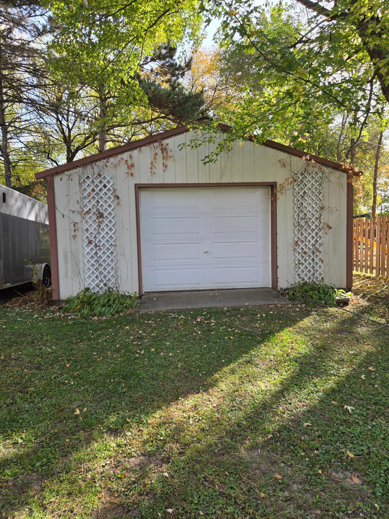 Detached pole building featuring an overhead garage door, concrete apron, and decorative lattice accents, offering excellent space for storage, hobbies, and recreational equipment.