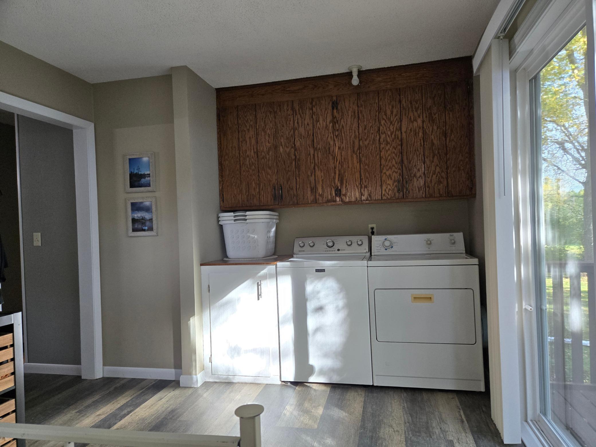Convenient main-level laundry area featuring a washer and dryer, abundant overhead cabinetry, additional storage, and natural light from the sliding glass door leading to the backyard.
