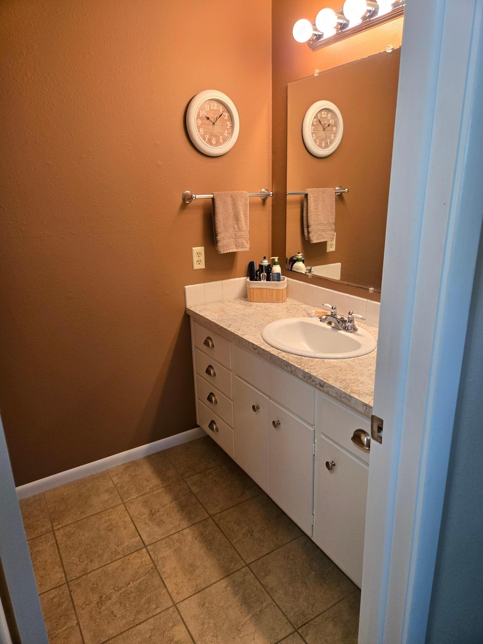 Convenient private half bath adjoining the primary bedroom, featuring a spacious vanity, ample cabinet storage, and tile flooring.