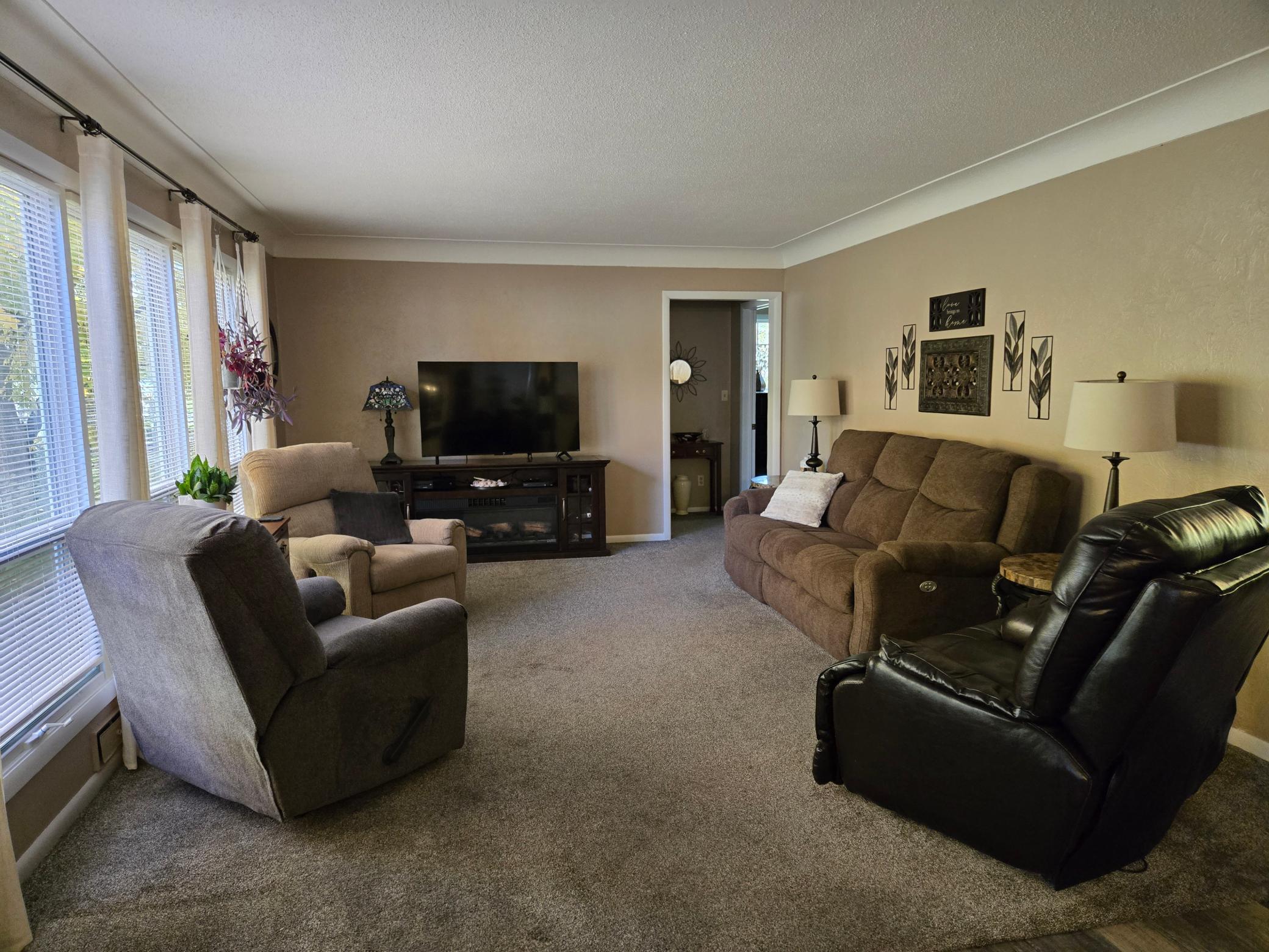 Spacious living room with abundant natural light from large windows, generous seating space, and a cozy atmosphere perfect for relaxing or entertaining.