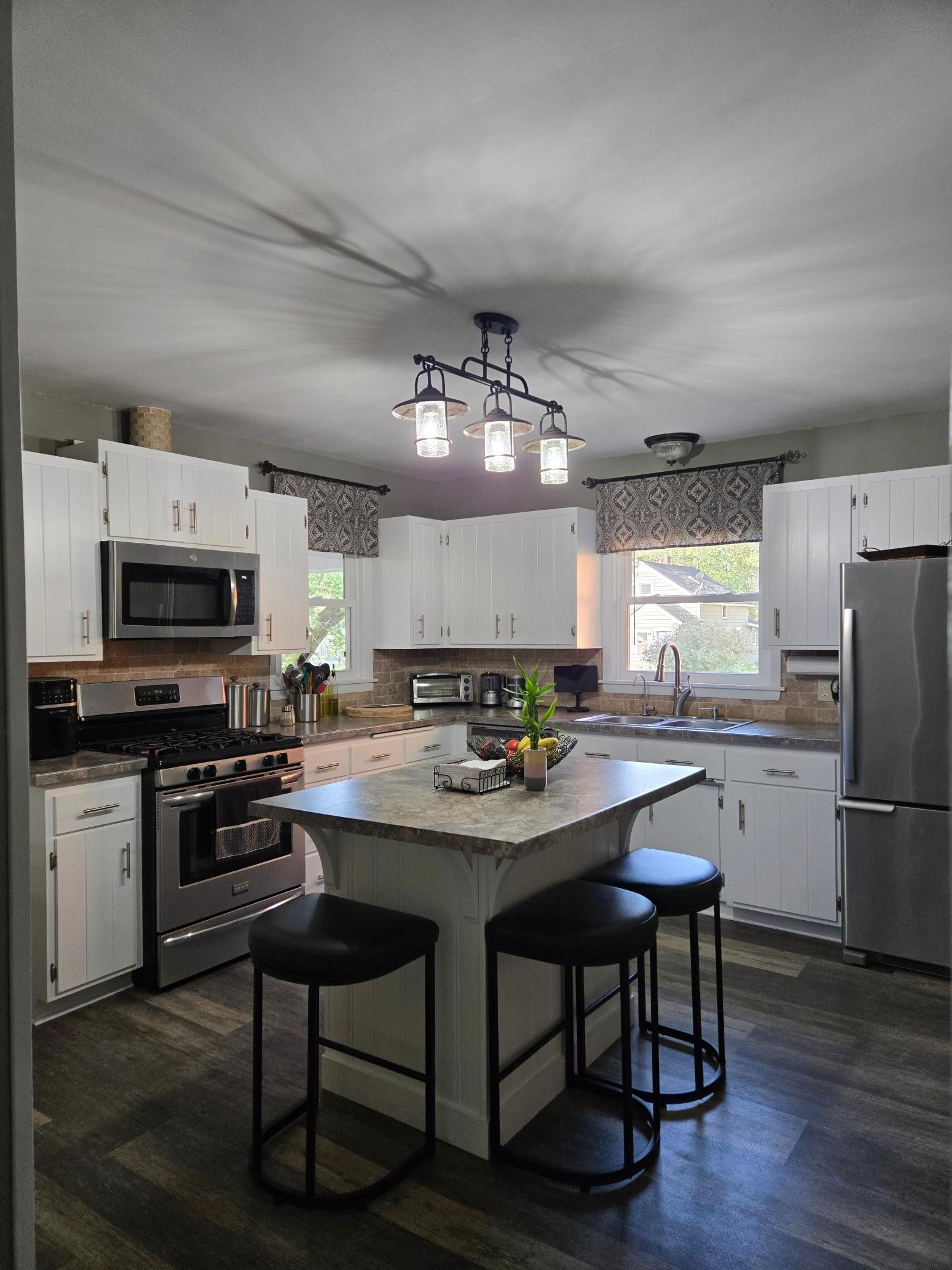 Bright and inviting kitchen featuring white cabinetry, stainless steel appliances, a center island with breakfast bar seating, attractive countertops, and updated lighting.