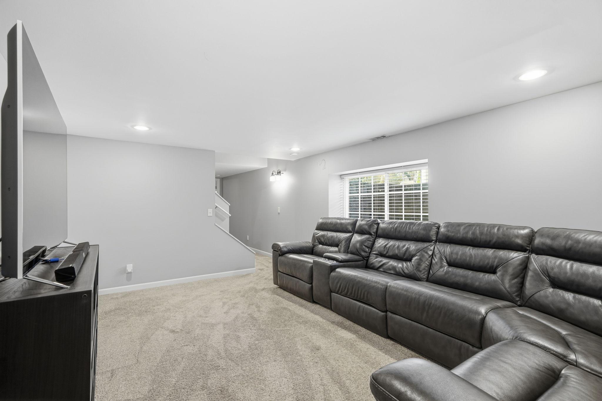 Lower-level family room area with neutral paint, recessed lighting and lush carpet!