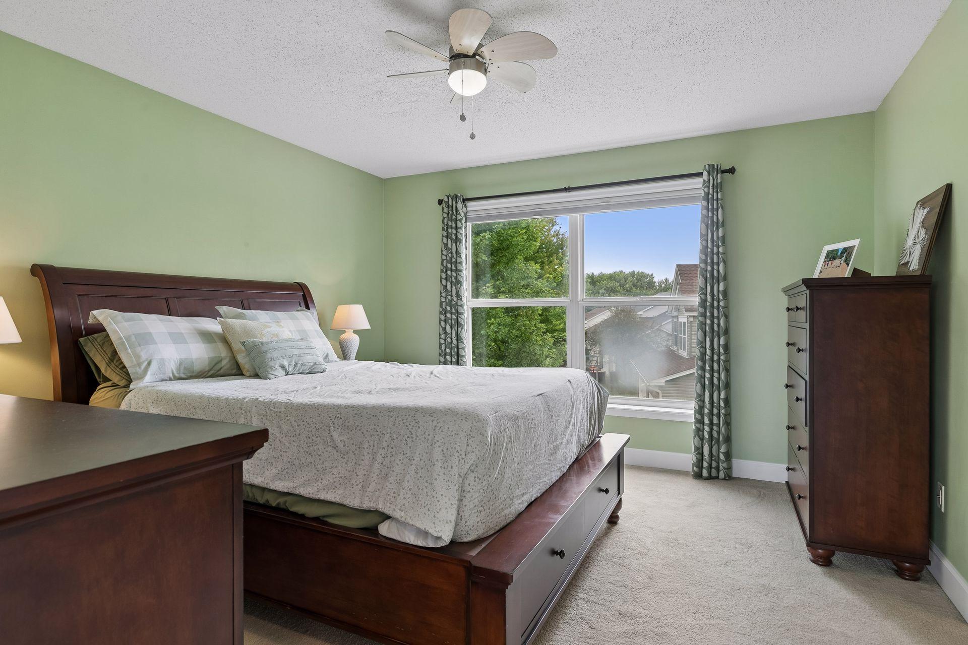 The spacious primary bedroom is filled with natural light from a large double window and offers soft carpet flooring, ample space and a ceiling fan with light.
