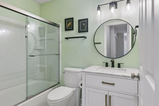 The updated (2023) upper level bathroom combines style and function with LVP flooring, a vanity, mirror with wall lights, and tub/shower combination.