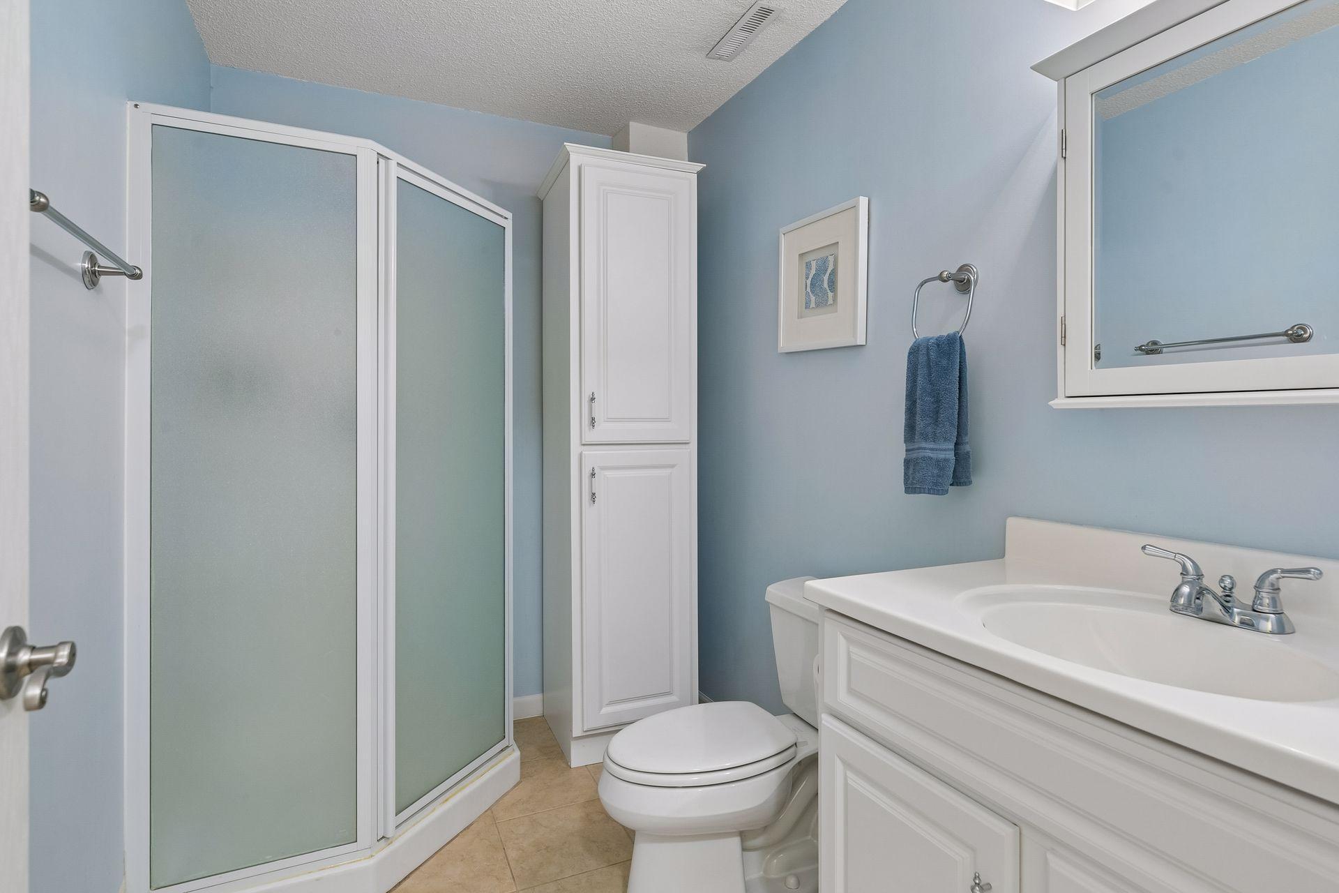 The lower level 3/4 bath provides a clean, functional space featuring tile flooring, vanity with mirrored medicine cabinet, wall lighting, and shower stall.