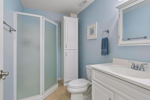 The lower level 3/4 bath provides a clean, functional space featuring tile flooring, vanity with mirrored medicine cabinet, wall lighting, and shower stall.