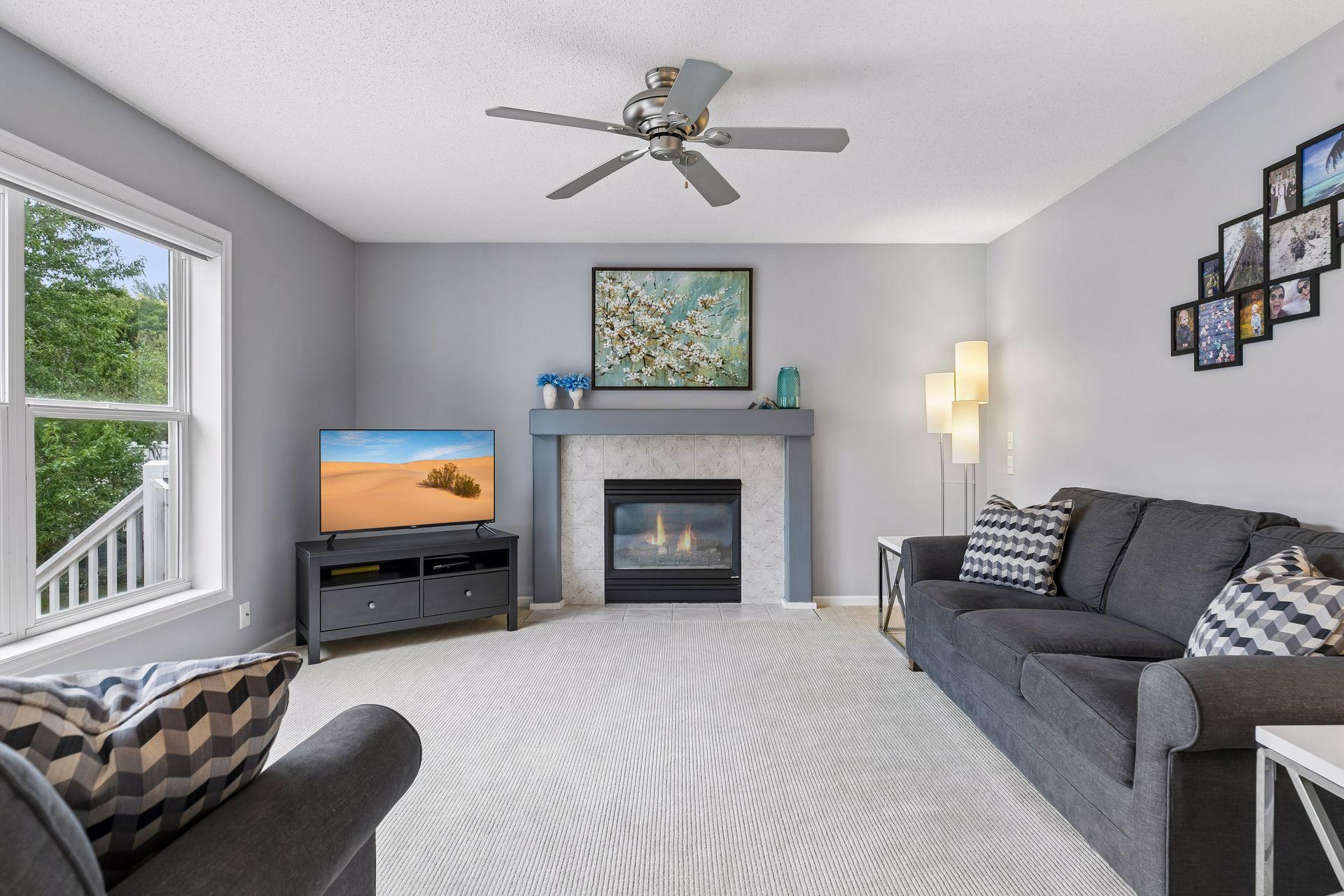 A gas fireplace creates a warm focal point in the spacious family room, complemented by carpet flooring, a ceiling fan, large windows, and ample room for relaxing or entertaining.