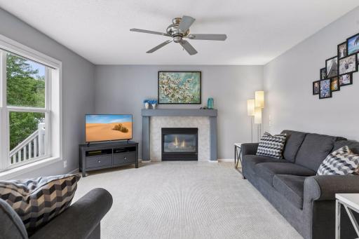 A gas fireplace creates a warm focal point in the spacious family room, complemented by carpet flooring, a ceiling fan, large windows, and ample room for relaxing or entertaining.