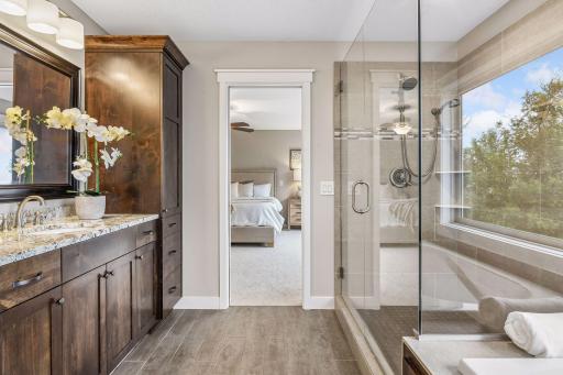 Spa-inspired primary bath with soaking tub, glass-enclosed shower, double vanity, and amazing treetop and lake views.