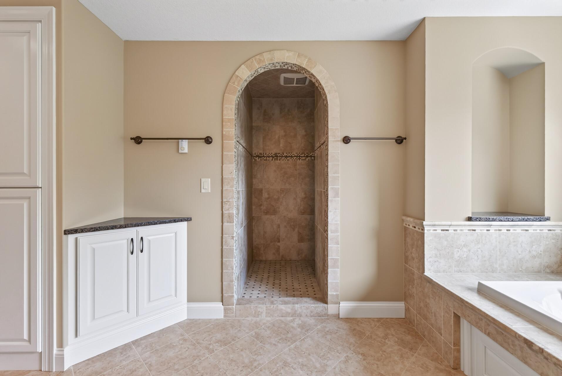 A graceful curved entry leads into the expansive tiled walk-in shower, adding architectural interest and a custom, spa-inspired feel to the primary bath.