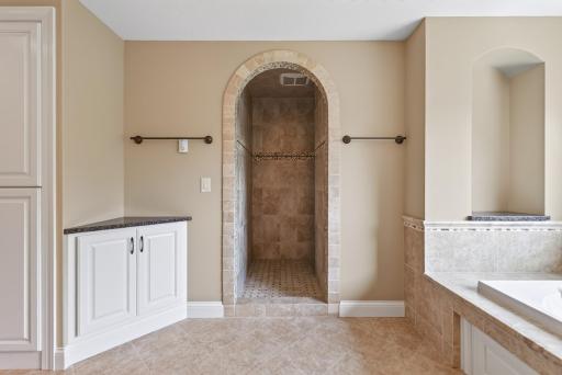 A graceful curved entry leads into the expansive tiled walk-in shower, adding architectural interest and a custom, spa-inspired feel to the primary bath.