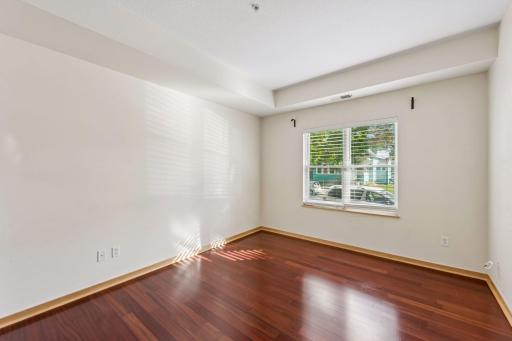 Bright second bedroom with a large window, wood flooring, and plenty of space for a bedroom or home office.