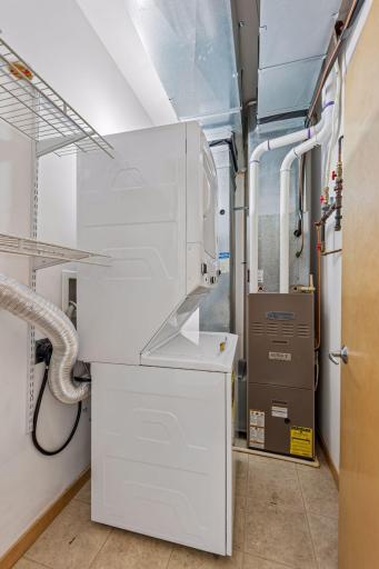 In-unit laundry and utility room with a stacked washer and dryer, plus additional shelving for convenient everyday storage.