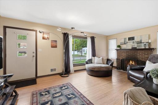 Spacious main-level living room featuring hardwood floors, a large picture window that fills the space with natural light, and a classic brick wood-burning fireplace.