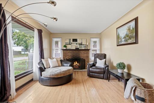 Inviting living room centers around the brick wood-burning fireplace, flanked by windows and complemented by beautiful hardwood flooring.