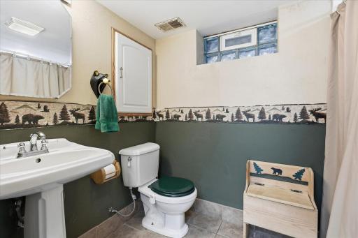 Convenient lower-level bathroom featuring a pedestal sink, tile flooring, and a glass block window.