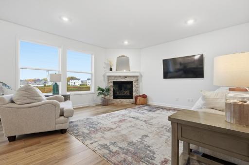 Bright and inviting living room featuring a cozy stone fireplace, abundant natural light, and peaceful views of open green space.