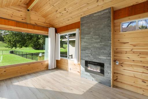 The home's sunroom features solid knotty pine paneling, stone fireplace, LVP flooring and lots of windows. Natural light fills this room all day long!