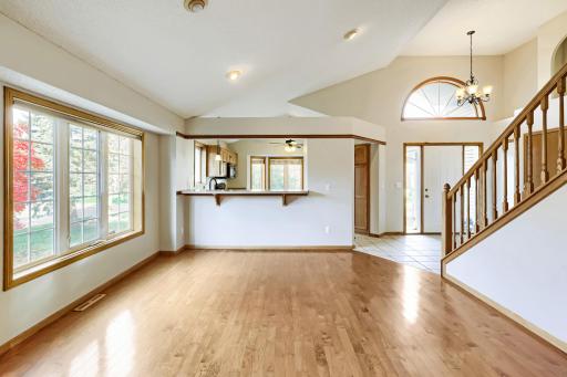 Sunny informal dining area open to the kitchen through a pass-through breakfast bar. Vaulted ceiling with recessed lighting, warm hardwood floors, and a large grid window overlooking the landscaped yard.