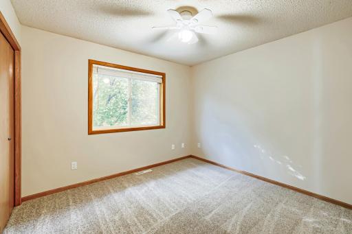 Bright and inviting second bedroom, one of three on the upper level, features fresh neutral paint, new carpeting, generous closet space, and a large window overlooking mature trees.