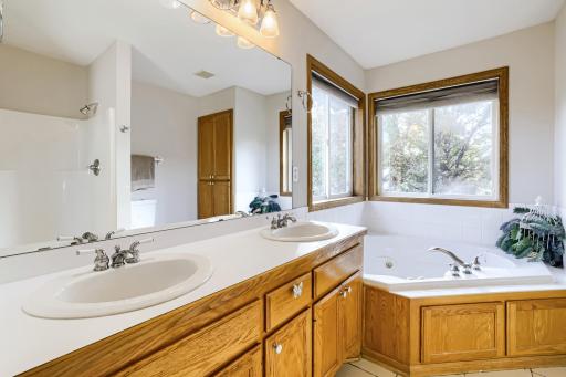 Spacious private primary bath features a double-sink vanity, relaxing jetted soaking tub surrounded by windows overlooking mature trees, separate shower, and abundant cabinet storage. Your own private retreat!