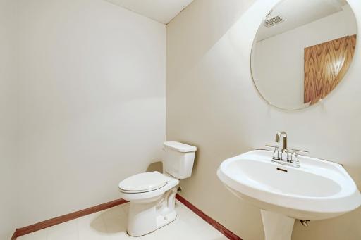 Convenient lower-level half bath located just off the spacious family room and wet bar area. Featuring a pedestal sink, stylish round mirror, and neutral finishes, it's a perfect addition for guests while entertaining!