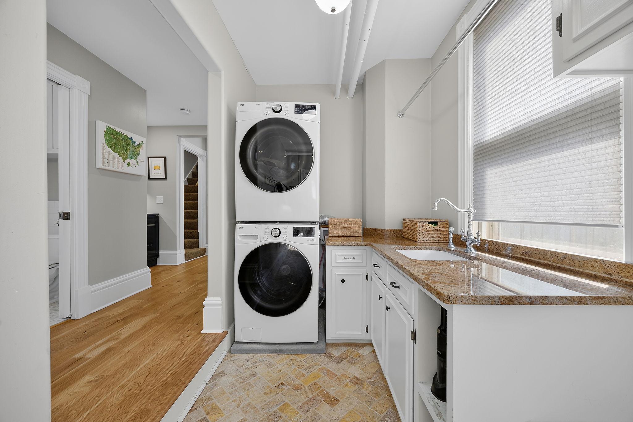 Completing the main level is a spacious mudroom and laundry room equipped with a front-loading washer and dryer, granite countertop and sink, built-in cabinetry, bench, and hooks, providing an organized and practical drop zone.