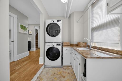 Completing the main level is a spacious mudroom and laundry room equipped with a front-loading washer and dryer, granite countertop and sink, built-in cabinetry, bench, and hooks, providing an organized and practical drop zone.