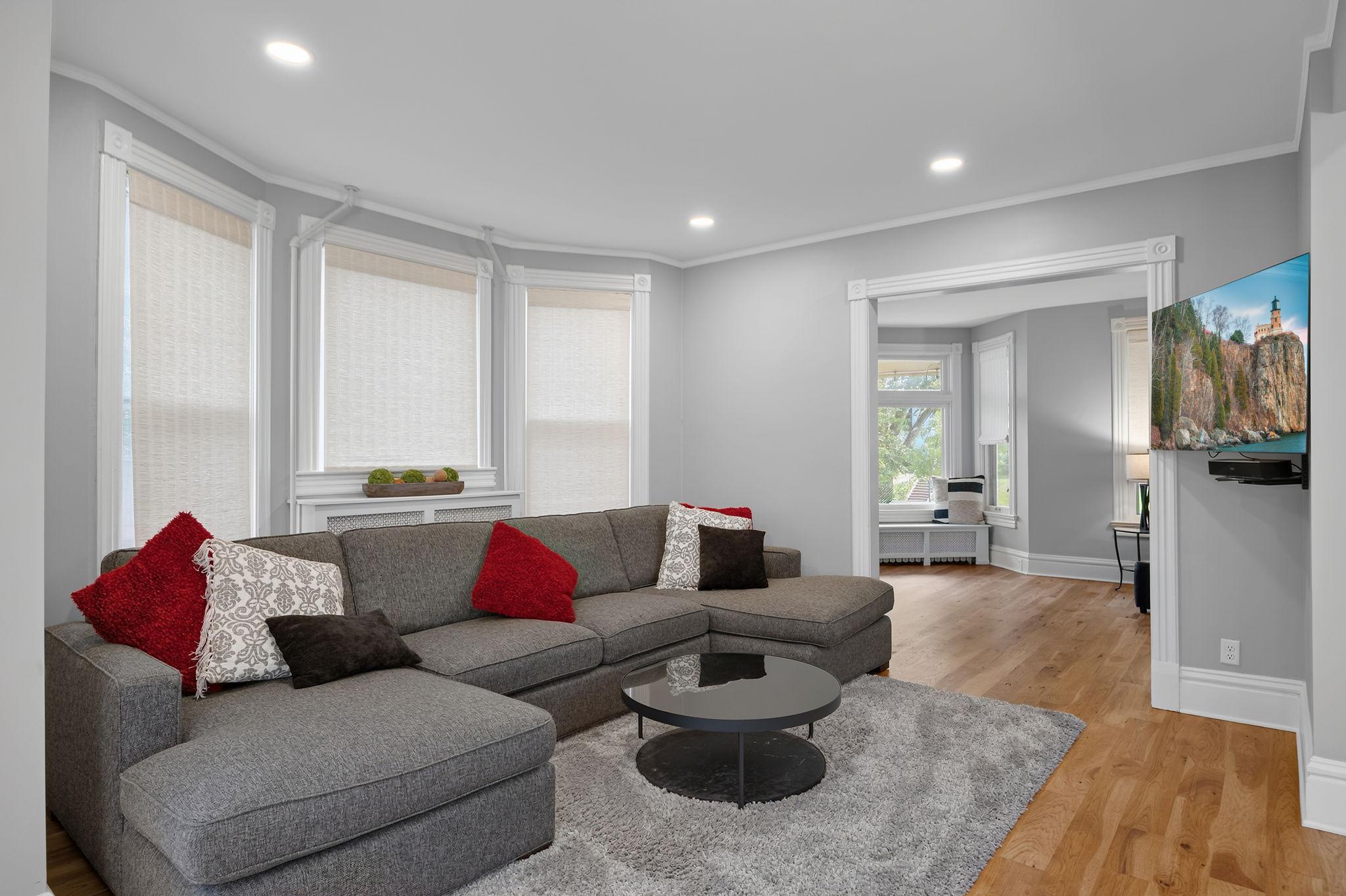 The nearby main-level living room showcases warm hardwood floors, recessed lighting, and a large bay window that fills the space with abundant natural light.