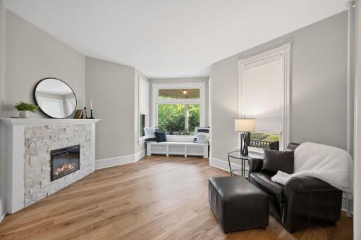 Just beyond the living room, a charming front sitting room offers an electric fireplace, large bay window with built-in bench seating, and views overlooking the wraparound porch and peaceful neighborhood.